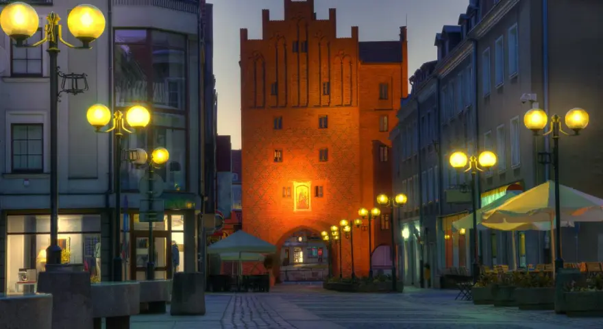 Brama miejska w Olsztynie o zmierzchu, oświetlona latarniami i iluminacją.