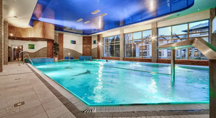 Basen hotelowy z niebieskim sufitem i dużymi oknami, woda w basenie jest turkusowa.