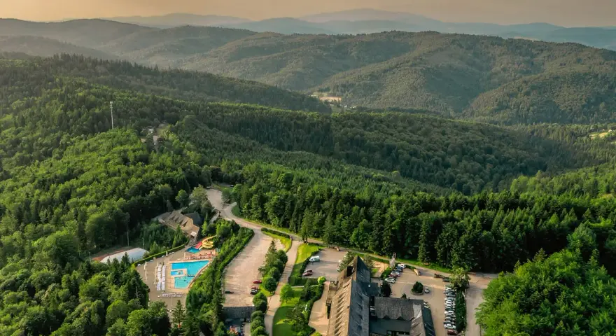 Widok z lotu ptaka na hotel SPA z basenem i zjeżdżalnią, otoczony lasem i górami.