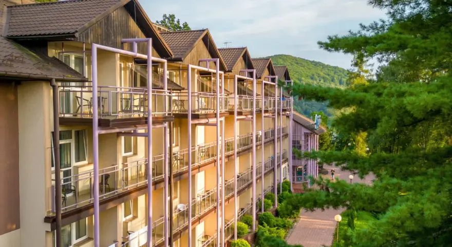 Hotel z balkonami w otoczeniu zieleni i gór.