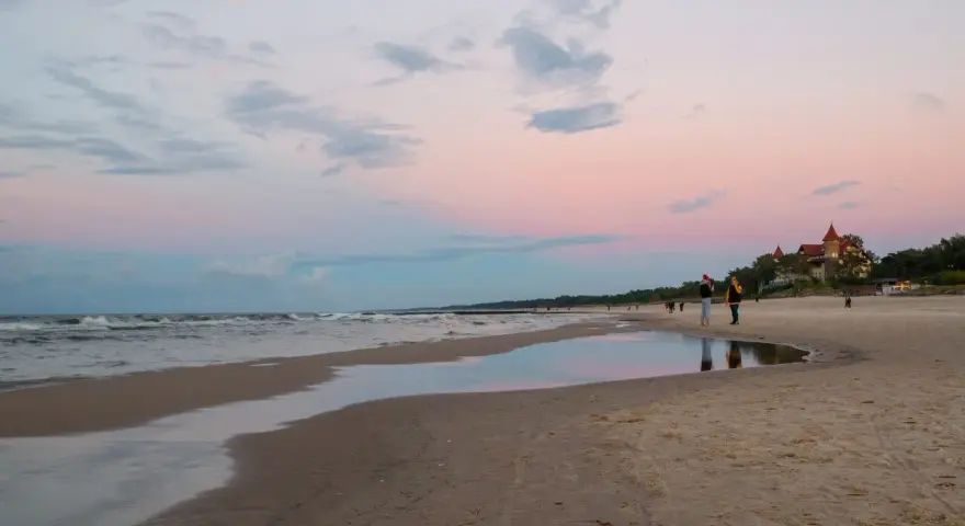 Plaża w Łebie o zachodzie słońca z widokiem na morze i budynek z czerwonym dachem.