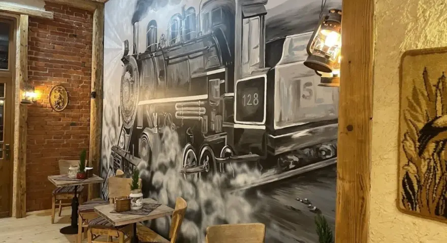 Wnętrze restauracji z muralem przedstawiającym lokomotywę i stoliki.