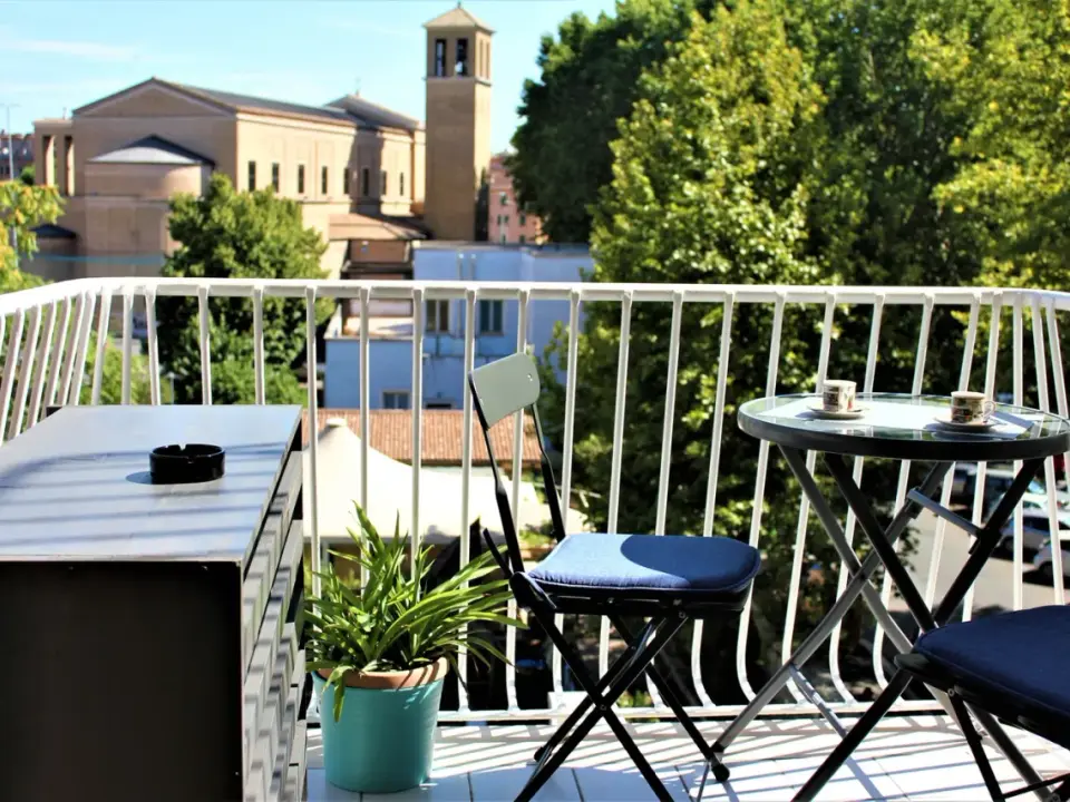 Balkon z widokiem na rzymskie budynki i zieleń, stolik z kawą.