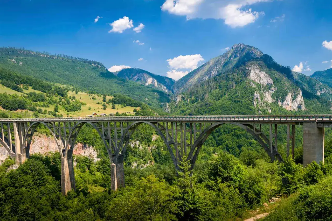 Most Durmitor: betonowy most łukowy nad zielonym kanionem, w tle góry i błękitne niebo.
